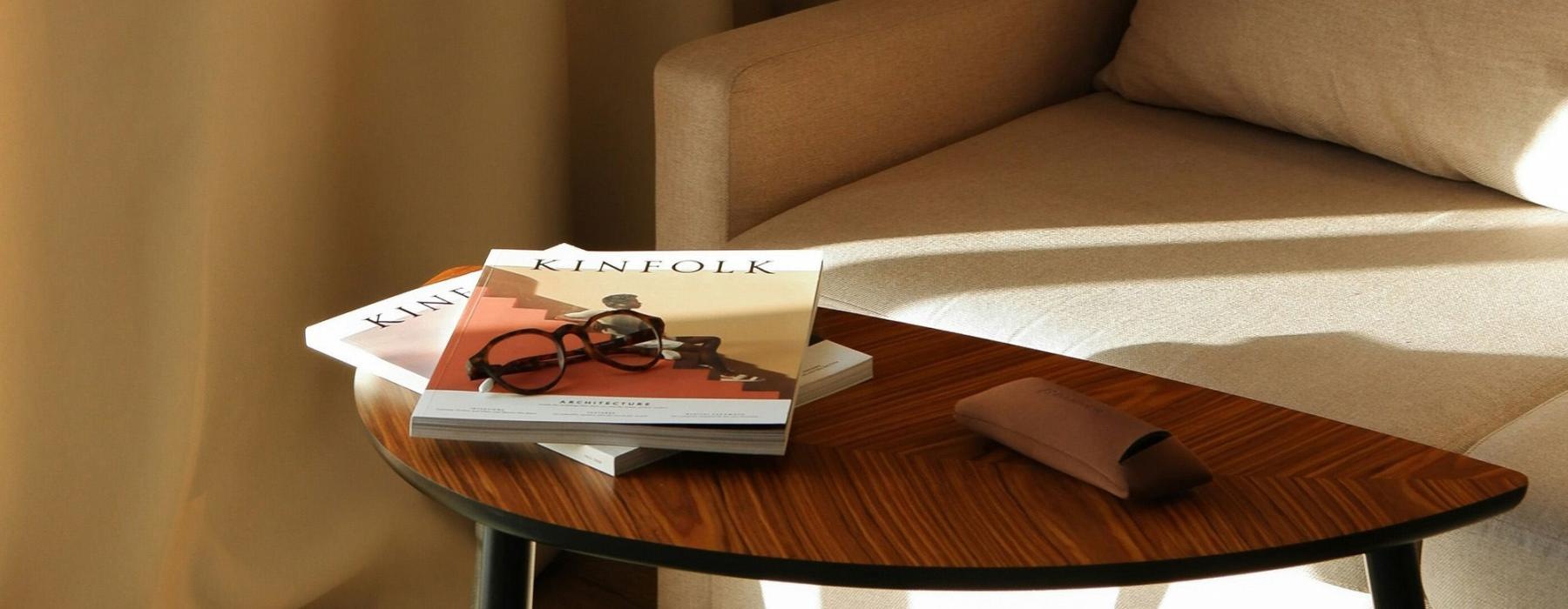A table with a book and glasses on it next to a couch in the sunlight.